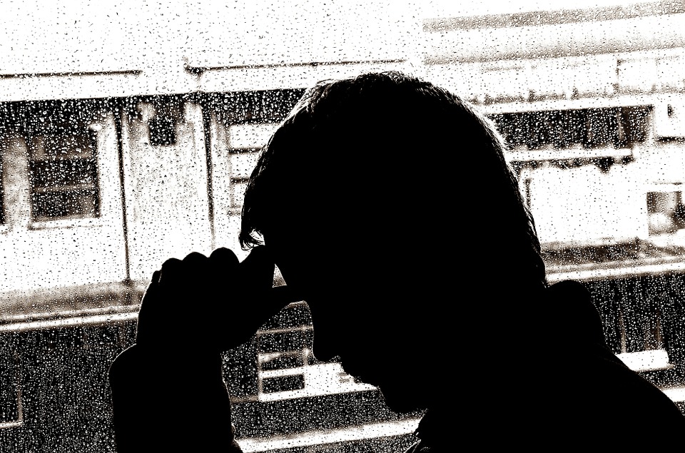 Silhouette of a man with his head in his hand and rain on the window