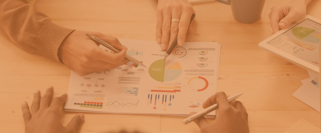 three people sat around a table looking at metrics on a tablet on printed graphs