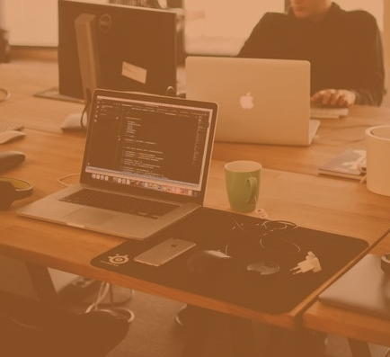 a desk with laptops, mobile phone, and headsets across them - with two people sat testing websites