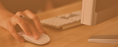 a hand using a mouse sitting in front of a keyboard and monitor