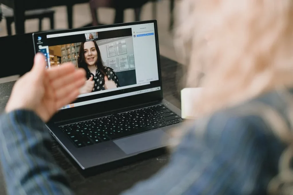 one lady sat at a desk signing to another lady on a laptop screen