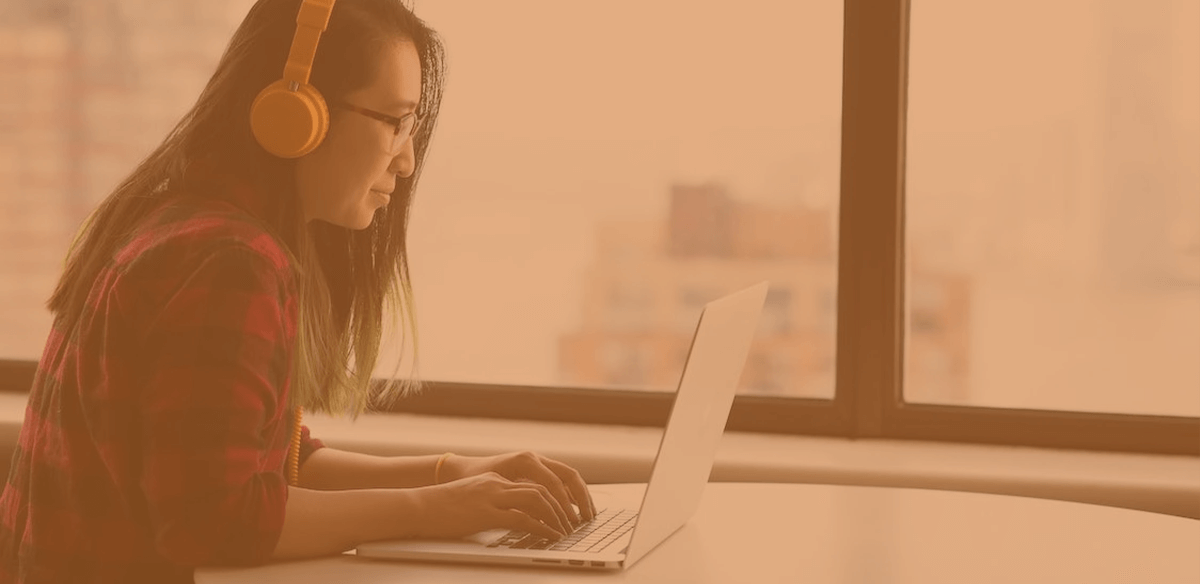 a student sat wearing an orange headset whilst typing on a laptop at a desk