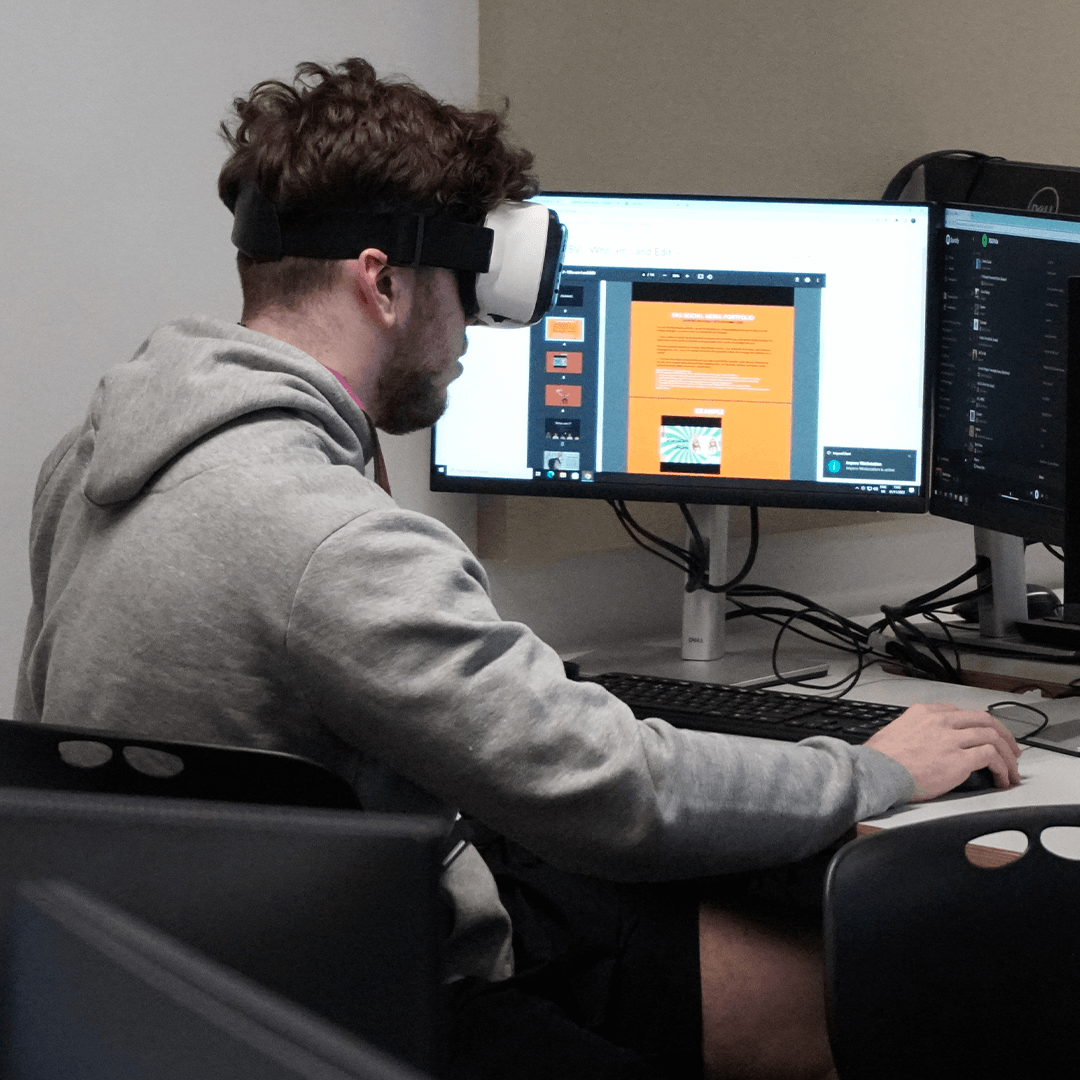 a student sat at a desktop computer with a VR headset on