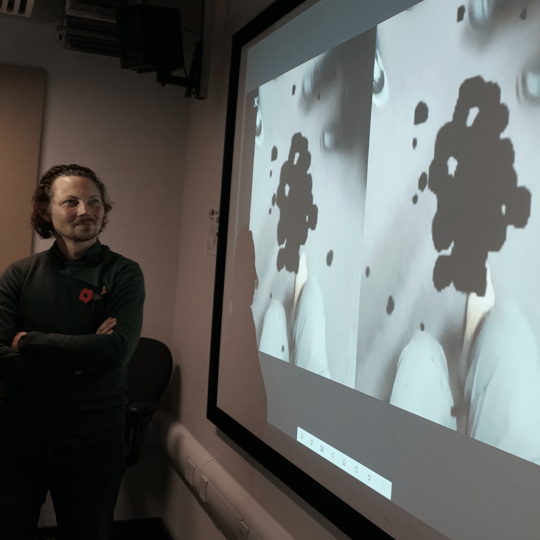 HeX Creative Director, James Hall, stood in front of a projector screen looking at a replicated visual impairment from the VR headset