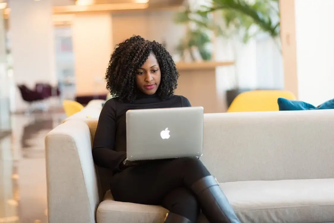A Black woman sat on a sofa using a laptop