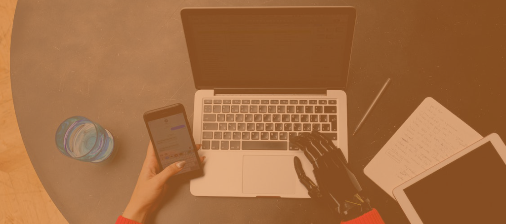 someone using a laptop with a black. prosthetic hand, and holding a mobile phone with their other hand