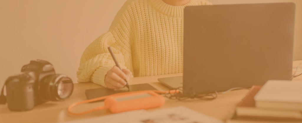 someone sat at a desk next to a camera, whilst creating a digital drawing on a laptop