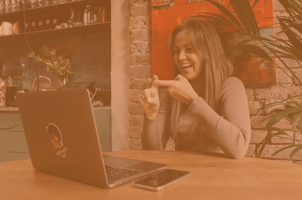 a woman sat laughing, whilst signing to someone on her laptop