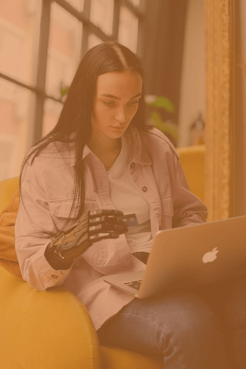 a woman sat on her sofa using a laptop with a prosthetic hand