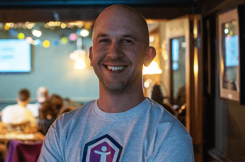Tom Miller smiling, wearing a t-shirt with a purple accessibility icon in the middle within a hexagon, at an Accessibility Nottingham event