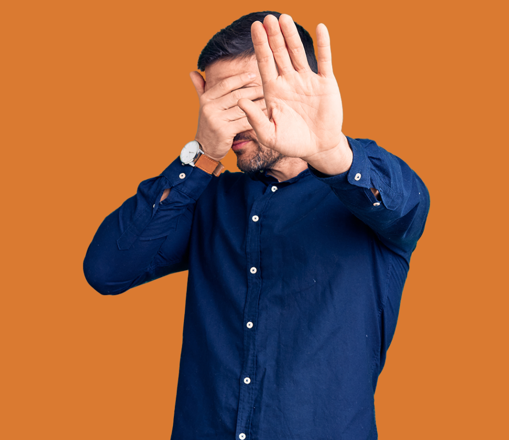 a man in a blue shirt is covering one eye with his hand and holding the other arm up to block seeing the screen