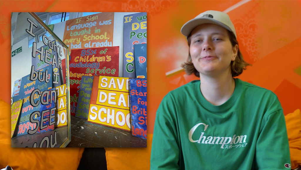 Zoe Milner sat wearing a green t-shirt and a cap on a sofa in HeX's office. Next to her is an image of a room full of her artwork stack against a wall.