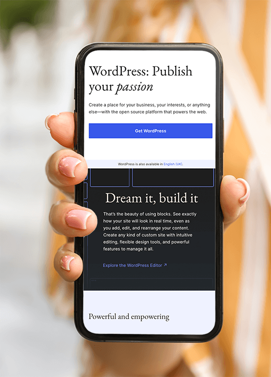 someone with pink painted nails holding up a black mobile phone. On the screen is the WordPress.org homepage, with text reading "Dream it, build it - That's the beauty of using blocks. See exactly how your site will look in real time, even as you add, edit and rearraange your content"