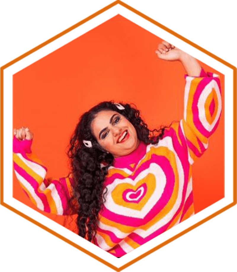 defeating disability's Bryony, is stood with her arms in the air wearing a bright striped top with white, pink, and yellow love hearts across it. Bryony has long black curly hair and has two large white hair clips on either side of her head. She is smiling against a bright orange backdrop.