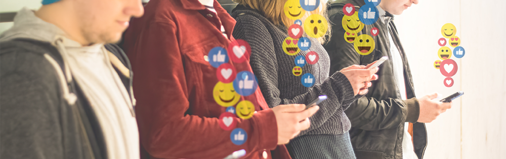 four people stood in a line using their mobile phones. Coming out of each phone are lots of different emojis.