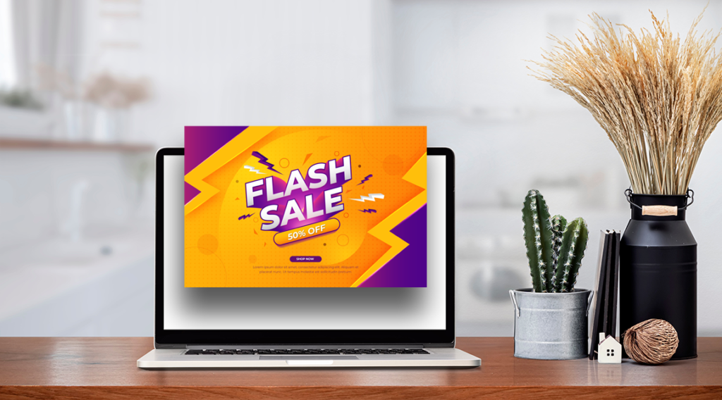 a silver laptop is on a wooden desk in someone's home next to a cactus and feathered plant. Coming out of the laptop's screen is a bright orange and purple pop-up advert, advertising a flash sale.