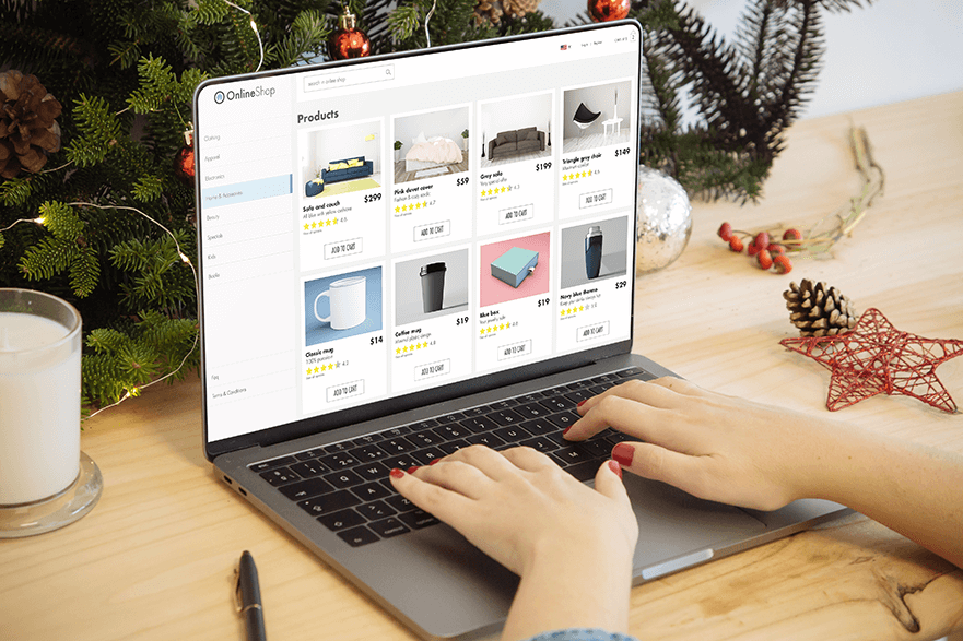 someone is typing into a laptop, on the screen is an online shop with various products and price tags. Behind the laptop is a Christmas tree and a glass of milk.