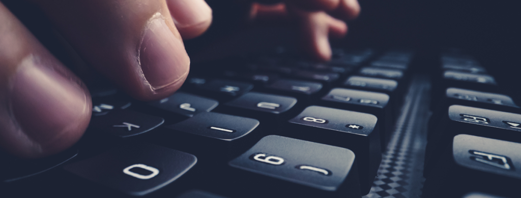 An up close shot of someone's fingers resting on a black keyboard in a darkened room