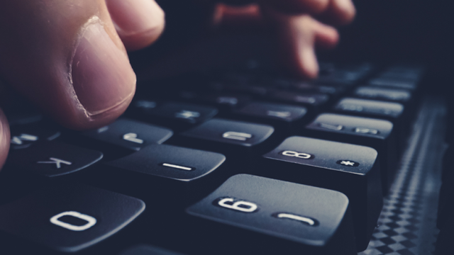 An up close shot of someone's fingers resting on a black keyboard in a darkened room