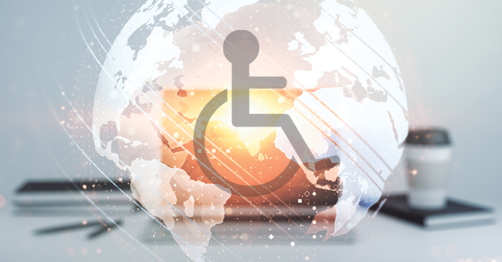 A laptop is on a grey desk. Emerging from the screen is a globe with a wheelchair user icon in the centre