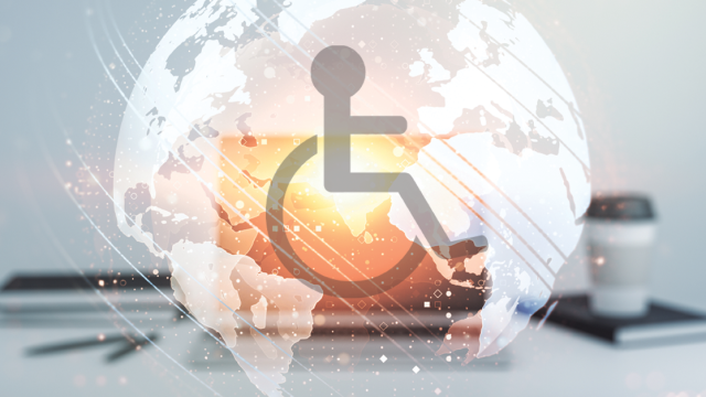 A laptop is on a grey desk. Emerging from the screen is a globe with a wheelchair user icon in the centre